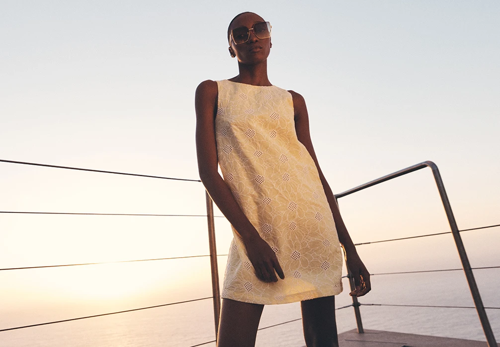 Model standing by a pier wearing the Floral Embroidered Cotton Mini Dress