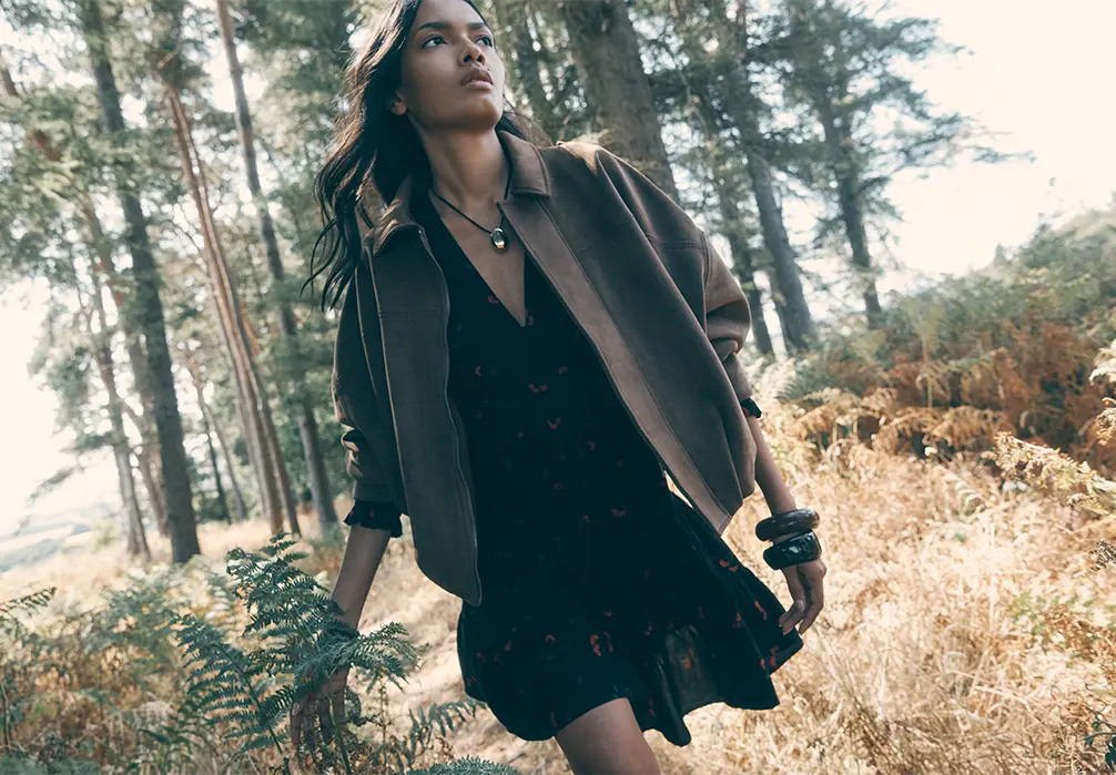 Model is sat wearing a brown suede bomber jacket with leopard print jeans