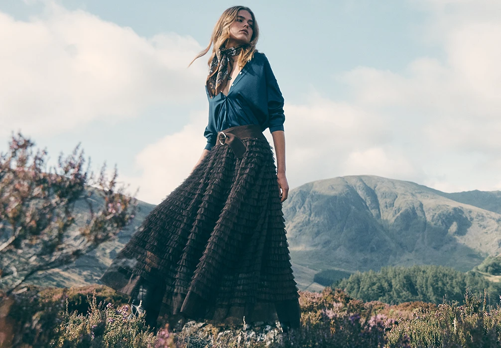 Model is outside wearing a satin blue shirt and brown ruffle maxi dress