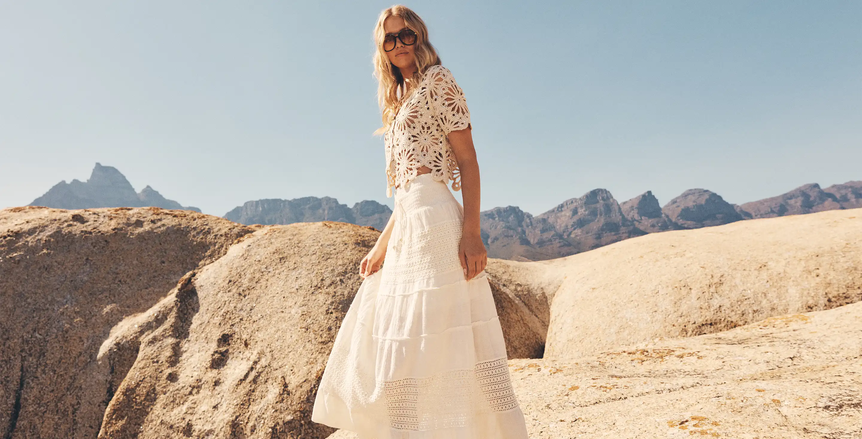 Model wearing a white crochet crop top and tiered maxi skirt in a desert landscape